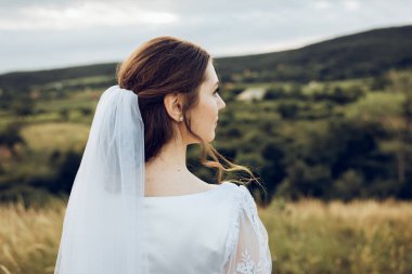 Doğanın ortasında beyaz elbiseli güzel bir gelinin fotoğrafı. Gelin elinde güzel bir buket tutuyor.
