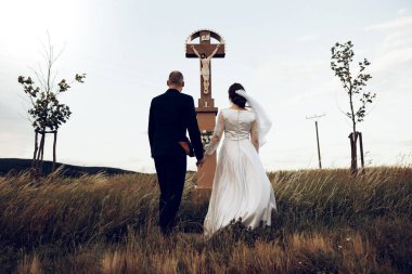 Gelin ve damat düğün çekimlerinde İsa 'nın heykeli önünde el ele tutuşuyorlar. Beyaz elbiseli güzel gelin ve şık damat.