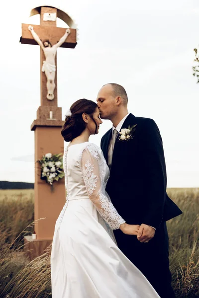 Gelin ve damat düğün çekimlerinde İsa 'nın heykeli önünde el ele tutuşuyorlar. Beyaz elbiseli güzel gelin ve şık damat.
