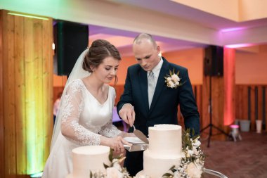 Yeni evliler düğün resepsiyonunda birbirlerinin pastalarını kesiyorlar. Çok güzel dekore edilmiş bir yerde. Düğün pastası, aşk, gelin.