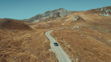 Areal shot over the Durmitor-national park of Montenegro.4K drone shot.Scenery of the steppe landscape and the rocky mountains in the background.Picturesque moony landscape.Car driving up to the hill.