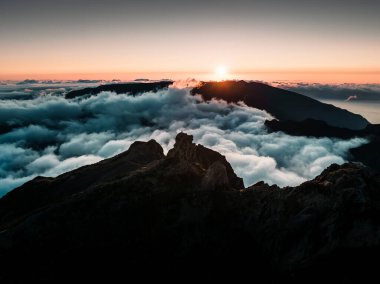 Drone 'dan çekilen, Pico Grande' den çekilen, güneş ışığıyla yıkanan bir manzara, bulutların altındaki görkemli dağlar.