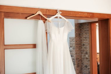 Sessizce bekleyen zarafet. Elbise daha giyilmemiş hayallerin sembolü olarak zarifçe asılmış. Yakında, gelini süsleyecek ve sonsuza dek onun başlangıcı olacak.