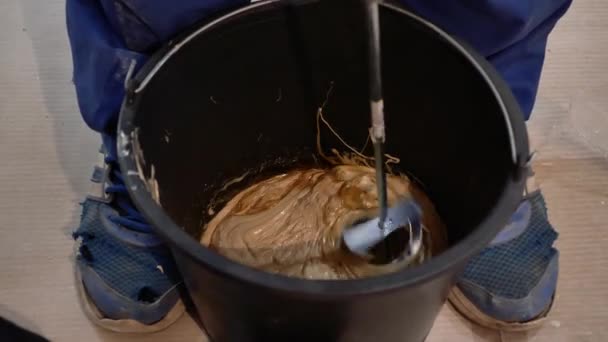 建设者浇灌 揉搓和称重胶水 施工搅拌机在工作 男人倒胶水 浓重的液体混在桶里 — 图库视频影像