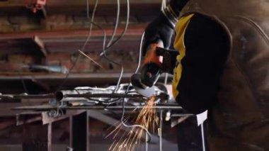 Bir adam dairesel testere ile çalışır. Açı öğütücü kullanıyor. Sıcak metalden kıvılcımlar uçuşuyor.