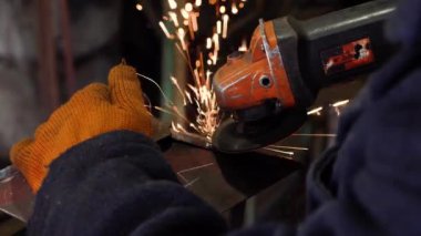 Bir adam dairesel testere ile çalışır. Açı öğütücü kullanıyor. Sıcak metalden kıvılcımlar uçuşuyor.