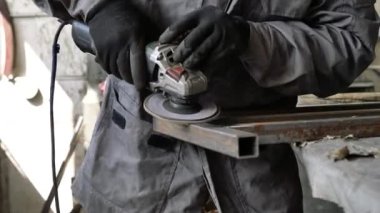 Bir adam atölyede metal öğütmek için özel bir alet kullanır. Bir endüstriyel işçiyle birlikte ağır bir makine fabrikasının içinde. Bir adam öğütme makinesiyle metal öğütüyor ve bir sürü kıvılcım uçuyor..