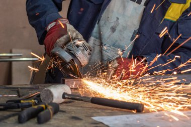 Bir adam atölyede metal öğütmek için özel bir alet kullanır. Bir endüstriyel işçiyle birlikte ağır bir makine fabrikasının içinde. Bir adam öğütme makinesiyle metal öğütüyor ve bir sürü kıvılcım uçuyor..