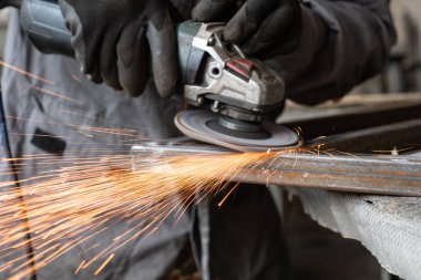 Bir adam atölyede metal öğütmek için özel bir alet kullanır. Bir endüstriyel işçiyle birlikte ağır bir makine fabrikasının içinde. Bir adam öğütme makinesiyle metal öğütüyor ve bir sürü kıvılcım uçuyor..