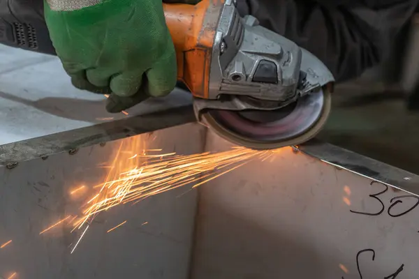 Bir adam atölyede metal öğütmek için özel bir alet kullanır. Bir endüstriyel işçiyle birlikte ağır bir makine fabrikasının içinde. Bir adam öğütme makinesiyle metal öğütüyor ve bir sürü kıvılcım uçuyor..