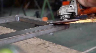 Bir adam atölyede metal öğütmek için özel bir alet kullanır. Bir endüstriyel işçiyle birlikte ağır bir makine fabrikasının içinde. Bir adam öğütme makinesiyle metal öğütüyor ve bir sürü kıvılcım uçuyor..
