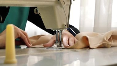 Dikiş. Yakın plan. Terzi dikiş makinesine kumaş dikiyor. Dikiş makinesinin iğnesi hareket halinde. Giysi fabrikasında çalışma süreci.