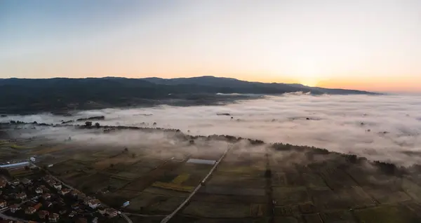 Foggy drone panorama over a village just before sunrise.