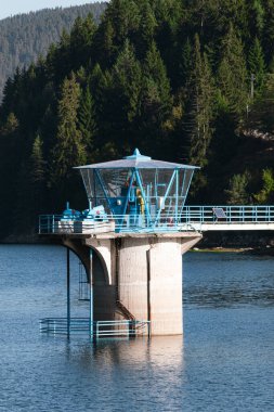 Arka planda çam ormanı ve köprü olan bir kontrol kabini..