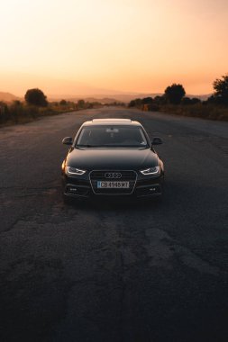 Bulgaria - 10 02 2024: Black Audi in the middle of an airport with vibrant orange light in the background. clipart