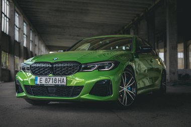 Bulgaristan - 09 09 09 2024: Boş bir otoparkta yeşil farları ve parlak tekerlekleri olan bir BMW 'nin ön fotoğrafı.