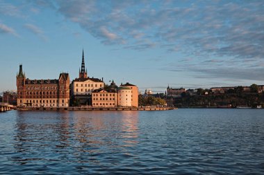 Stockholm, İsveç - Eylül 2022: Riddarholm Kilisesi (Riddarholmskyrkan), Riddarholmen Adası ve şehir merkezinden gün batımına doğru ufuk çizgisi manzarası