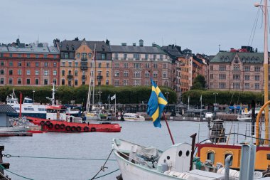 Stockholm, İsveç - Eylül 2022: Rıhtıma bakan renkli şehir manzarası Yabancılar ve Skeppsholmen 'den bayrak taşıyan gemiler