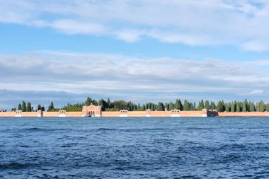 Venedik, İtalya - 9 Kasım 2023: Venedik 'teki San Michele Mezarlığı' nın sakin dalgalı deniz suyunun kıyılarında yeşil ve sonbahar ağaçları bulunan manzarası
