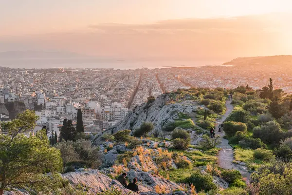 stock image Athens, Greece - March 02, 2024: Athens cityscape and sea at sunset from Philopappos hill