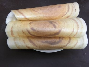 Güney Hint yemeklerini bembeyaz bir tabakta sergileyen üç lezzetli dosa.