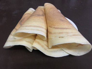 Beyaz bir tabağa istiflenmiş, Güney Hint yemeğini temsil eden bir masaya yerleştirilmiş üç altın-kahverengi domates.