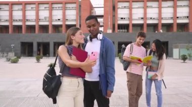 Cep telefonunu kullanan ve ekrandaki bir şeye işaret eden genç bir kadının yan görüntüsü sınıf arkadaşına kampüs konseptinde onunla yürüyen komik bir şey gösteriyor: üniversite hayatı.