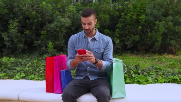 Joven Sonriente Sentado Calle Con Bolsas Compras Hablando Por Teléfono — Vídeos de Stock