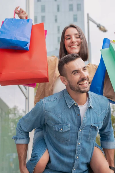 vertical photography caucasian man carrying his girlfriend on his back having fun together carrying shopping bags Concept of excitement, weekend and family.