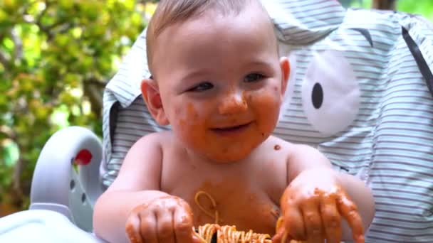 美しい赤ちゃんは 食べるためにスパゲッティをつかむときに混乱を作ることを楽しんでいます 自家製パスタとトマトソースで楽しいドリンク — ストック動画