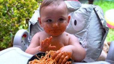Kıymetli bebek elleriyle spagetti yiyerek ortalığı kirletmekten hoşlanıyor. Ev yapımı makarna ve domates soslu komik bebek.