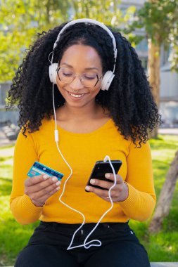 Dikey fotoğraf çeken mutlu siyah kadın kredi kartı ve akıllı telefonu elinde. Konsept: çevrimiçi alışveriş