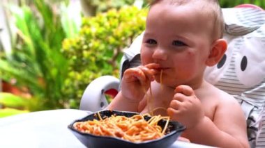 Güzel bebek elleriyle spagetti yemekten zevk alıyor. Ev yapımı makarna ve domates sosuyla eğlenceli bir içecek.