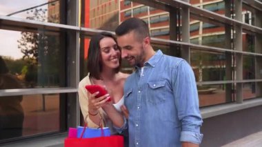 Çevrimiçi alışveriş yapan genç bir çift, açık havada akıllı telefonları olan satışları bulmaktan mutlu. Gençler cep telefonuyla sosyal medya uygulaması kullanarak eğleniyorlar. Akıllı telefon izleyen arkadaşlar..