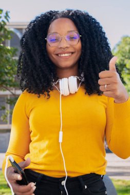 Yakın plan mutlu kıvırcık saçlı, gözlüklü genç kadın başparmağını kaldırıyor. Mutluluğun yüz ifadesi. 