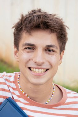 Kampüste oturan beyaz bir öğrenci kameraya bakıp gülümsüyor. Üniversite hayatı konseptine bakıyor..