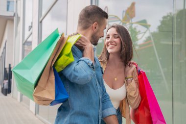 Alışveriş merkezinde mutlu genç yetişkinler. Gülen beyaz bir adam ve alışveriş çantası taşıyan bir kadının portresi.