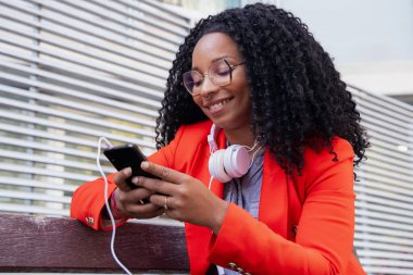 Gözlüklü güzel siyahi kadın dışarıda cep telefonunda sosyal medya uygulaması kullanarak gülümsüyor. Cep telefonunda sohbet eden kız. Cep telefonunda sohbet eden kız..