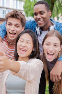 Bir grup arkadaş üniversitede selfie çekiyor ve birlikte gülüyorlar. Teknoloji ya da ağ kurma, bağlantı ve mutlu üniversiteliler sosyal medyaya gülümserken fotoğraf çekiyorlar.