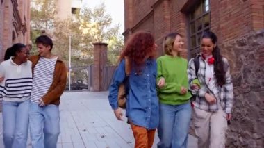 Üniversite kampüsünde sarılıp gezen ve dışarıda gülen çok ırklı bir grup öğrenci. Gençler birlikte eğleniyor..
