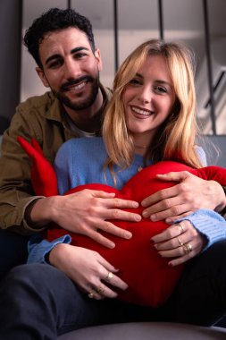 Dev bir kalple gülümseyen genç çift kameraya bakıyor. Sevgililer Günü.