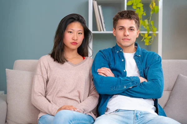 Close-up Angry young multiracial man and woman with cell phone posing looking at camera during meeting on sofa at home.