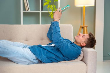 Genç yetişkin, kolay ve güvenli elektronik ödemeler yapmak için internet üzerinden mutlu bir alışveriş yapmak için kanepeye uzandı.