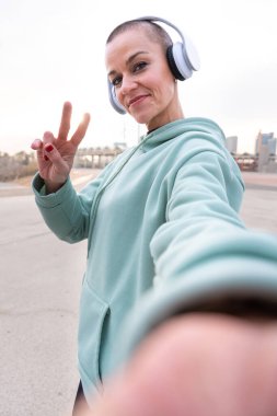 Sportif bir kadın ara veriyor. Cep telefonuyla fotoğraf çekiyor. Kameraya bakıyor.