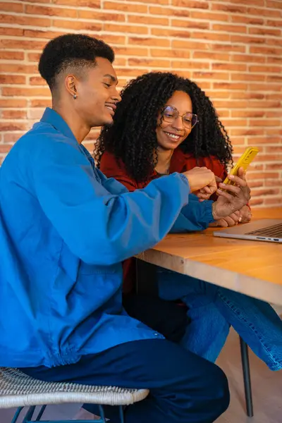 A multiethnic couple using a cell phone makes each other smile at home, a Latino boyfriend and an African-American girlfriend on social media try out a new mobile app. Young people work with laptop