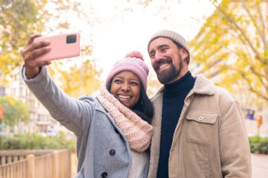 Akıllı telefondan fotoğraf çeken mutlu arkadaşlar dışarıda eğleniyorlar. Eşler moda bir alışveriş merkezinde hafta sonunun tadını çıkarıyorlar.
