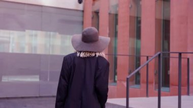 Şapkalı ve çantalı mutlu kadın ofisin girişine doğru yürüyor..