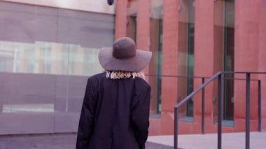 Şapkalı ve çantalı mutlu kadın ofisin girişine doğru yürüyor..