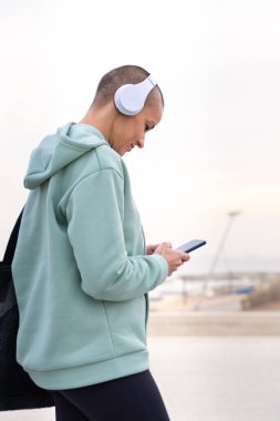 Egzersiz yapmaktan yorgun düşmüş kulaklıklı atletik bir kadın cep telefonu mesaj uygulamasını kullanmak için ara veriyor..