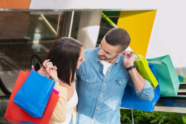 Mutlu arkadaşlar ellerinde çantalarla alışveriş merkezinde yürüyen merdivene çıkıyorlar.